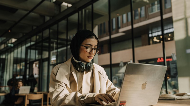 A focused woman wearing a headscarf works on her laptop in a stylish urban cafe., tags: bulgarien für - pexel
